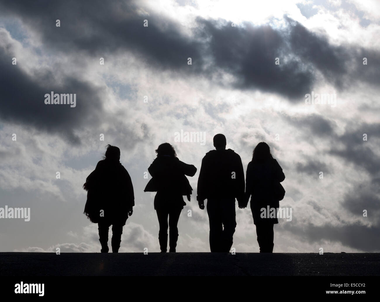 Four silhouetted people walk into the clouds Stock Photo