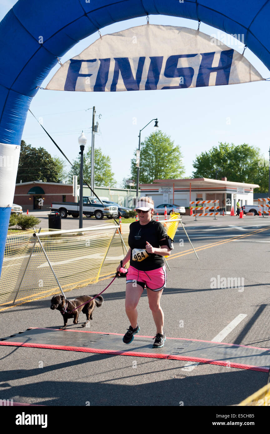 Woman in 5K or 10K marathon race crossing finish line with a dog on leash Stock Photo