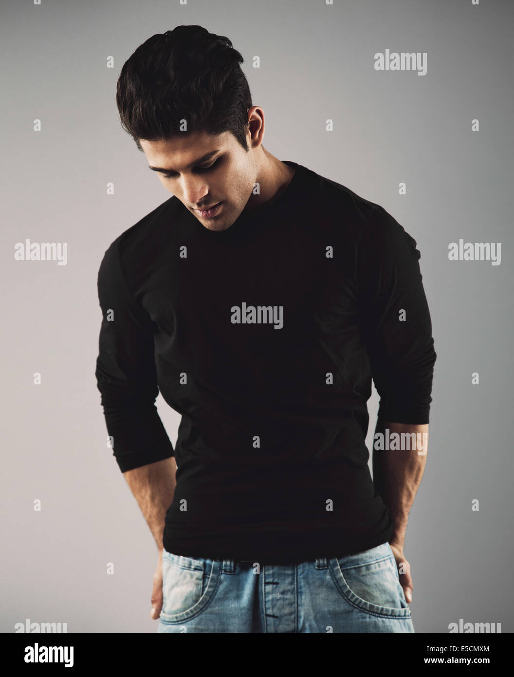 Portrait of hispanic young man standing on grey background looking down thinking. Stock Photo