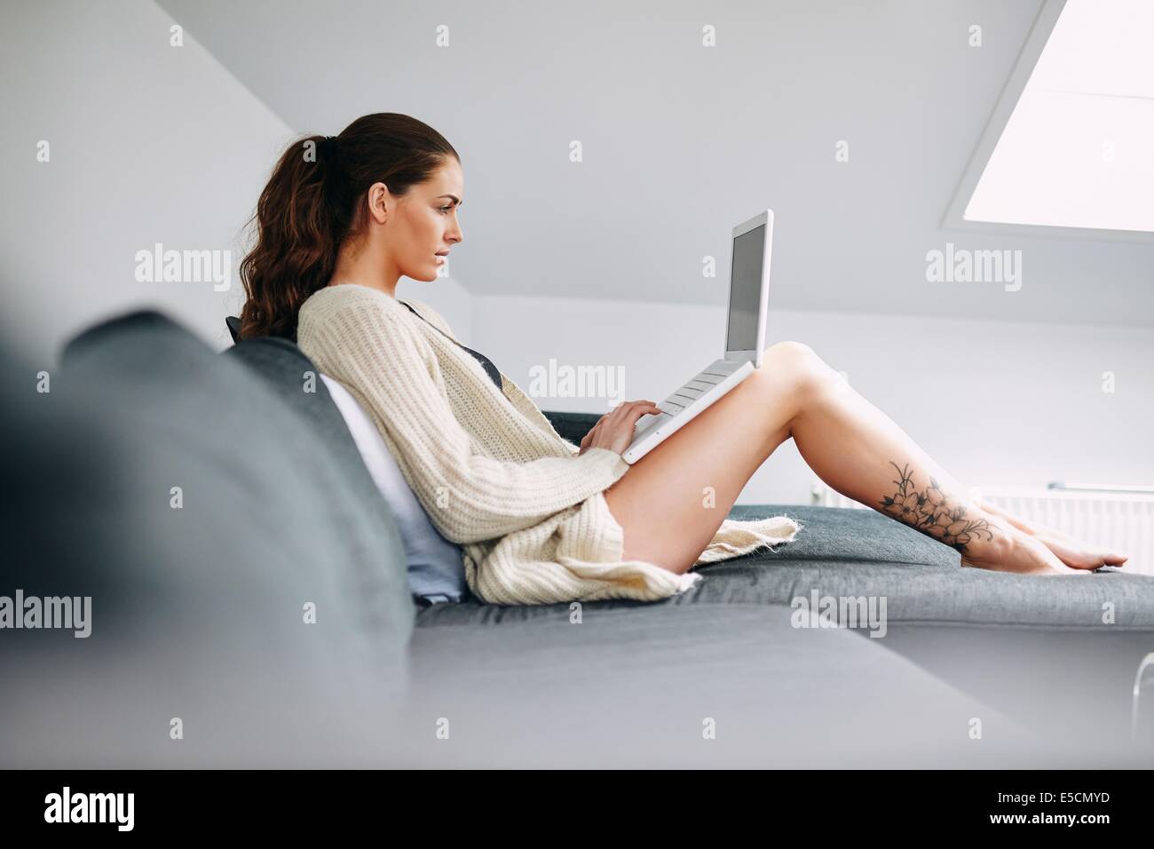 Side View Of Young Lady Sitting On Sofa Using Laptop Caucasian