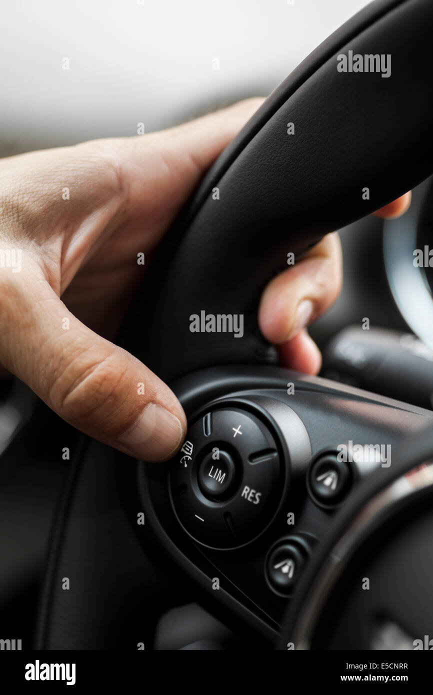 A hand pushes the cruise control button on a steering wheel Stock Photo