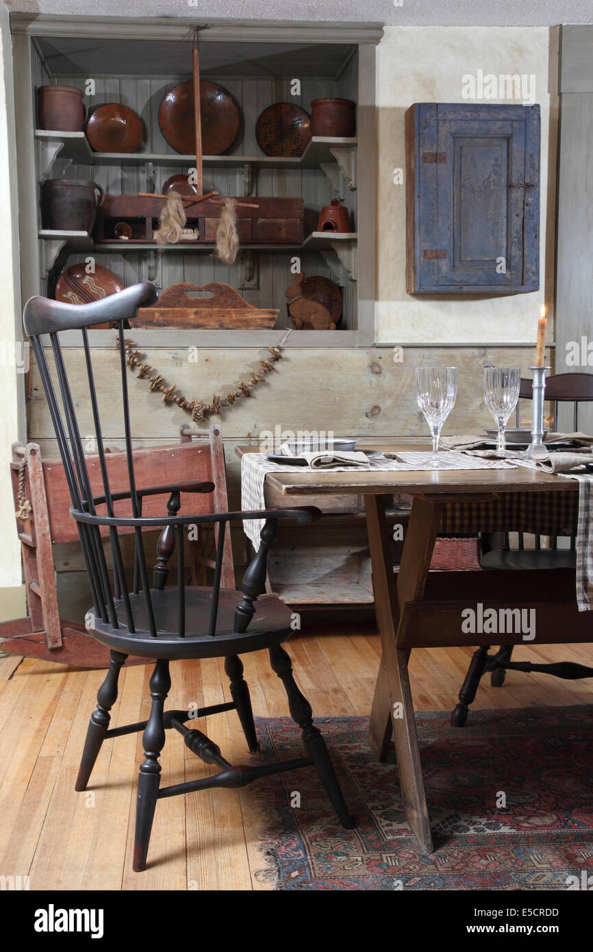 Rustic style dining room with table and chair. In the background a wall cabinet and old plates, USA. Stock Photo