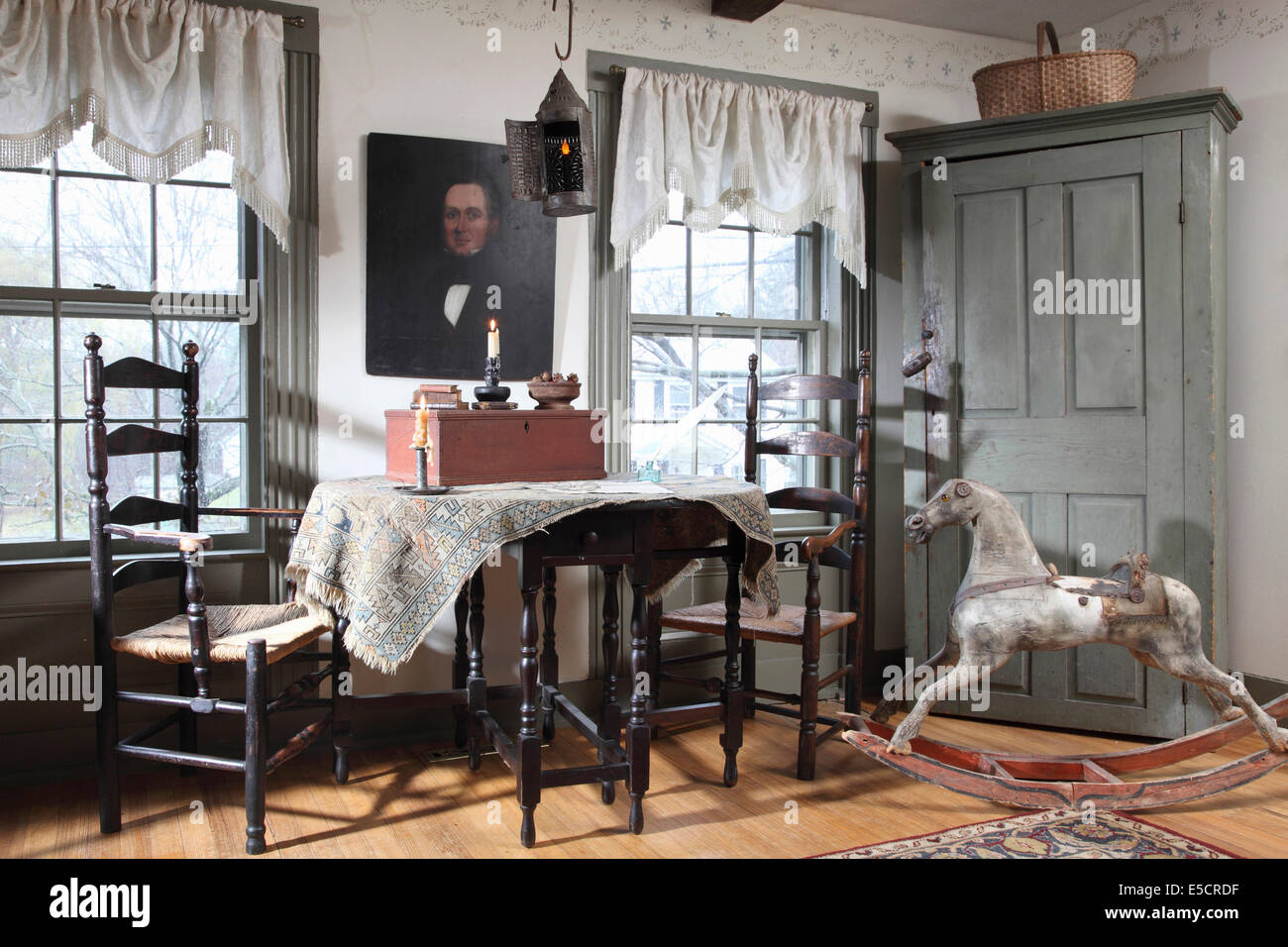 An informal diining room with table chairs and Rustic corner cabinet. Also in the room is an old rocking horse and a portrait Stock Photo
