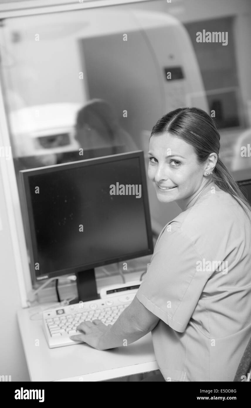 Young female doctor smiling working at monitor of mri machine scanner. Stock Photo