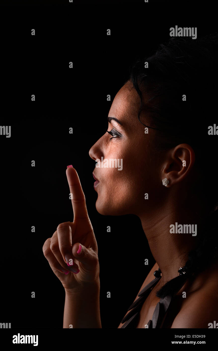 Profile of young woman asking for silence in front of black background Stock Photo