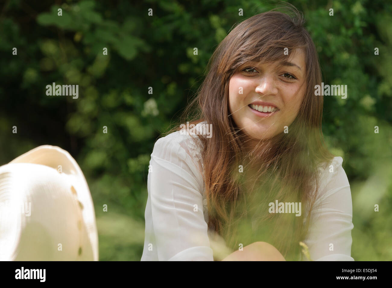 Portrait of smiling young woman sitting on wooden bench in a garden ...
