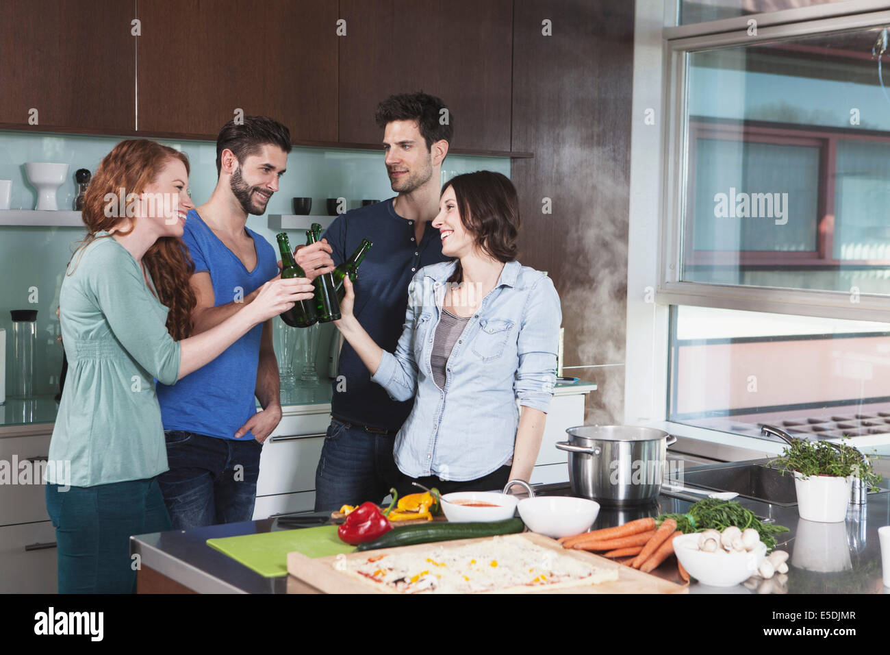 Portrait of four friends toasting with beer bottles in a kitchen Stock Photo