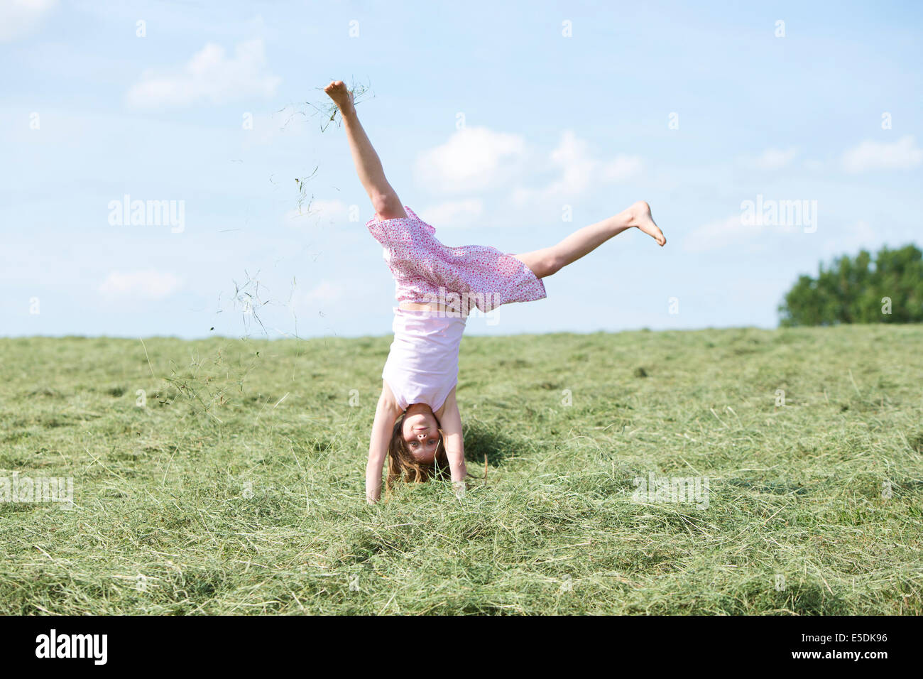 Germany, Bavaria, Young girl doing a cartwheel on meadow with hay Stock Photo
