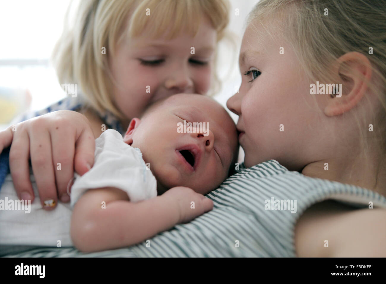 Two little girls kissing their newborn brother Stock Photo