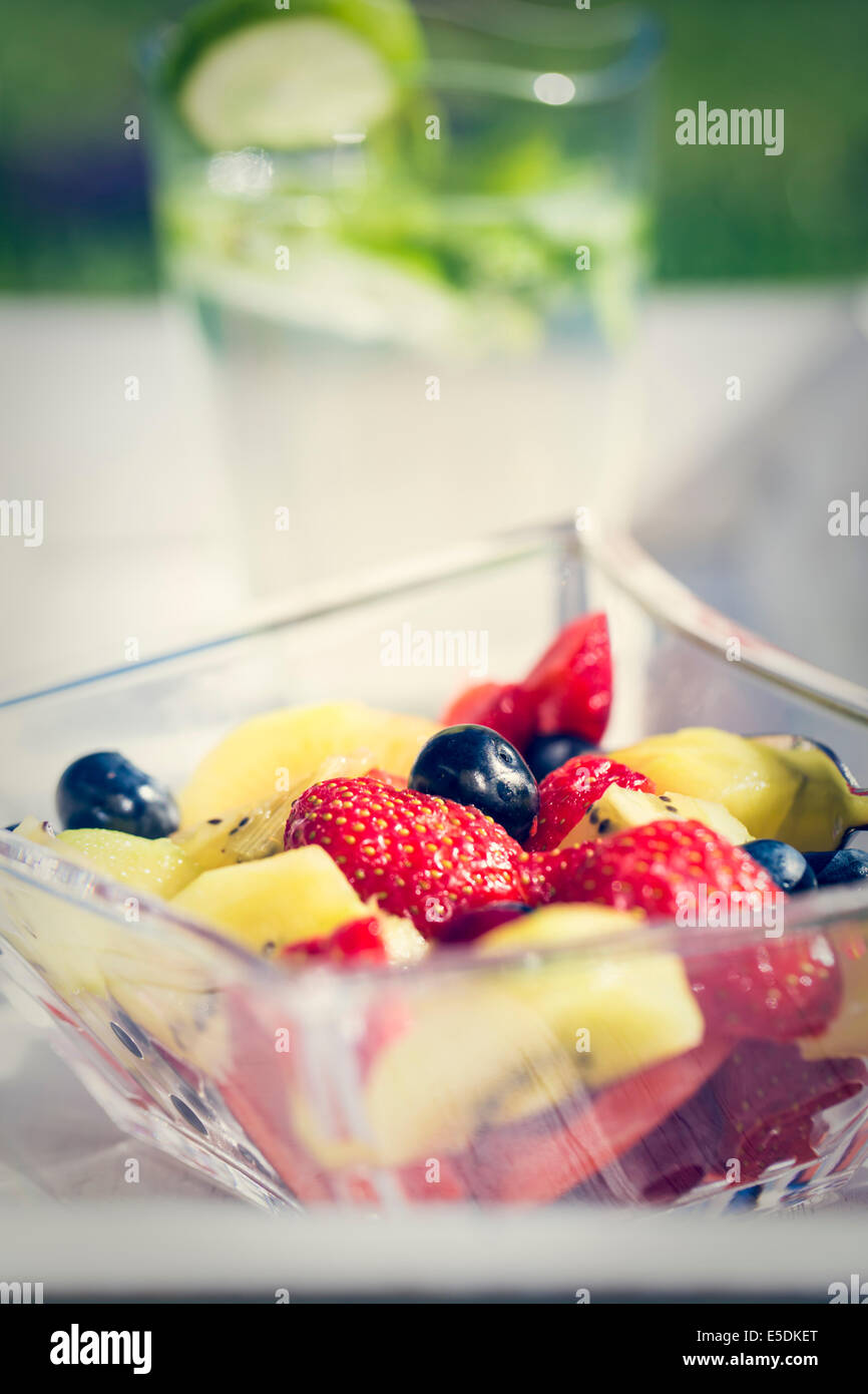 Glass bowl of fruit salad and glass of lime lemonade in the background