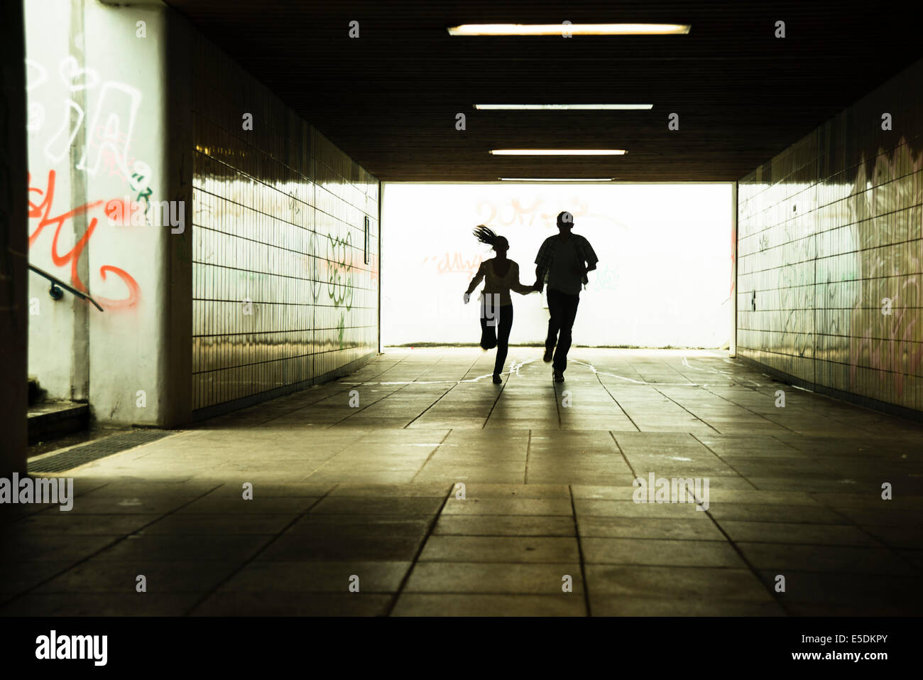 Young couple running together in a dark underpass Stock Photo