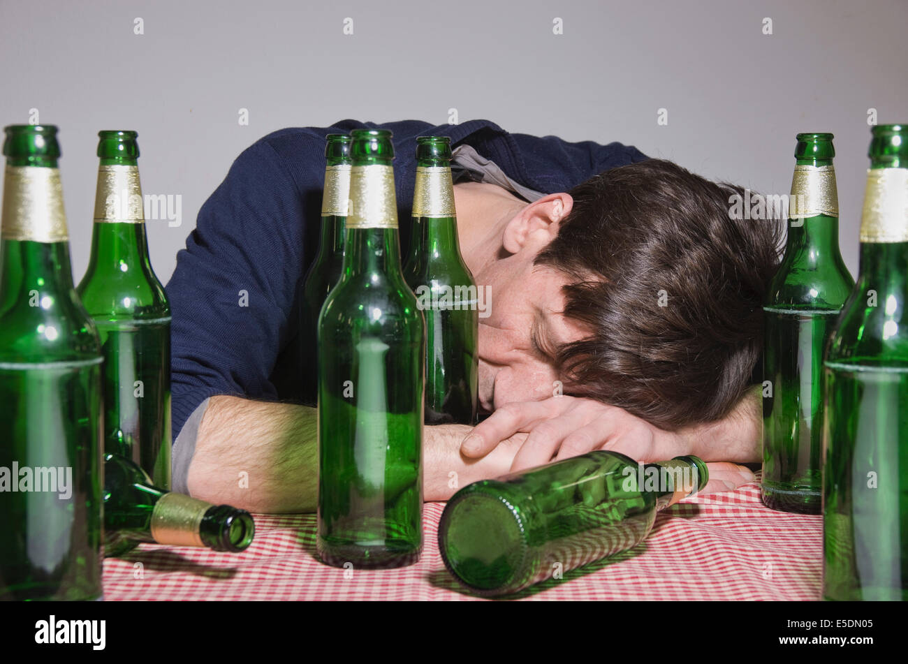 Man lying on table surrounded by beer bottles Stock Photo
