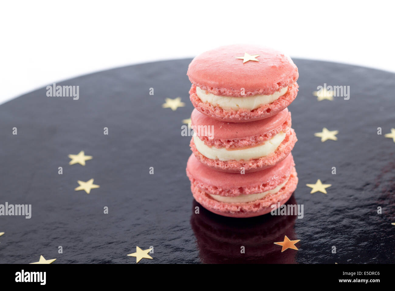 Three pink macarons on a black shiny surface with golden stars Stock Photo