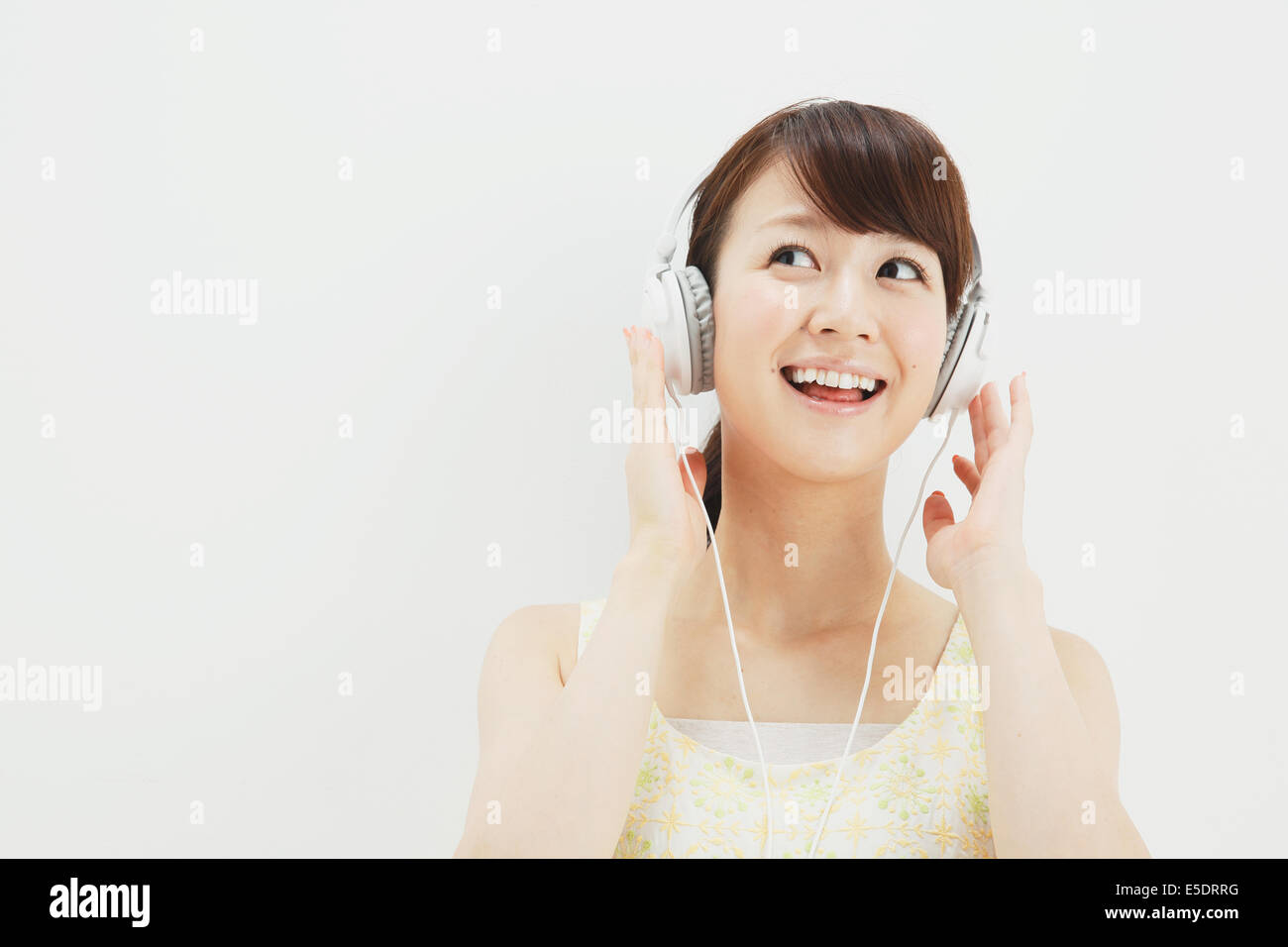 Japanese young woman in a one piece dress with earphones standing against white background Stock