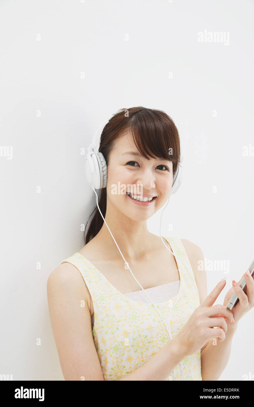 Japanese young woman in a one piece dress with earphones standing against white background Stock