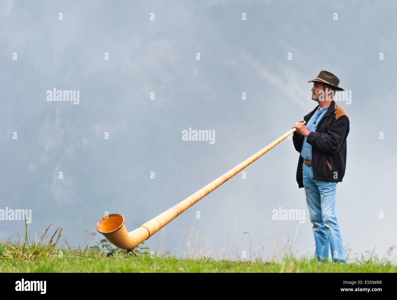 A Swiss alphorn player standing on a mountain ridge, about to start playing Stock Photo