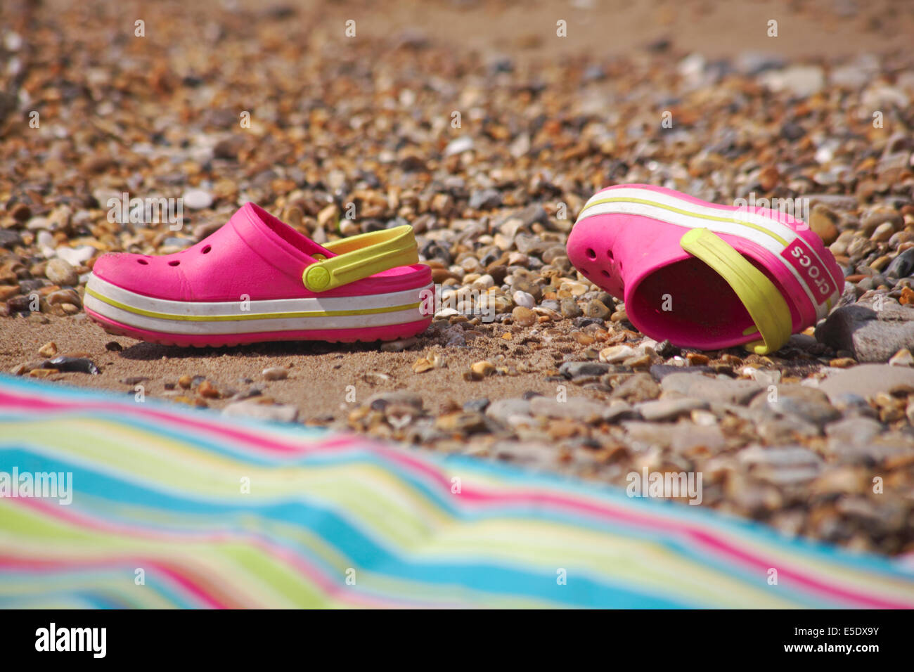 pink crocs discarded on beach next to stripey beach towel Stock Photo ...