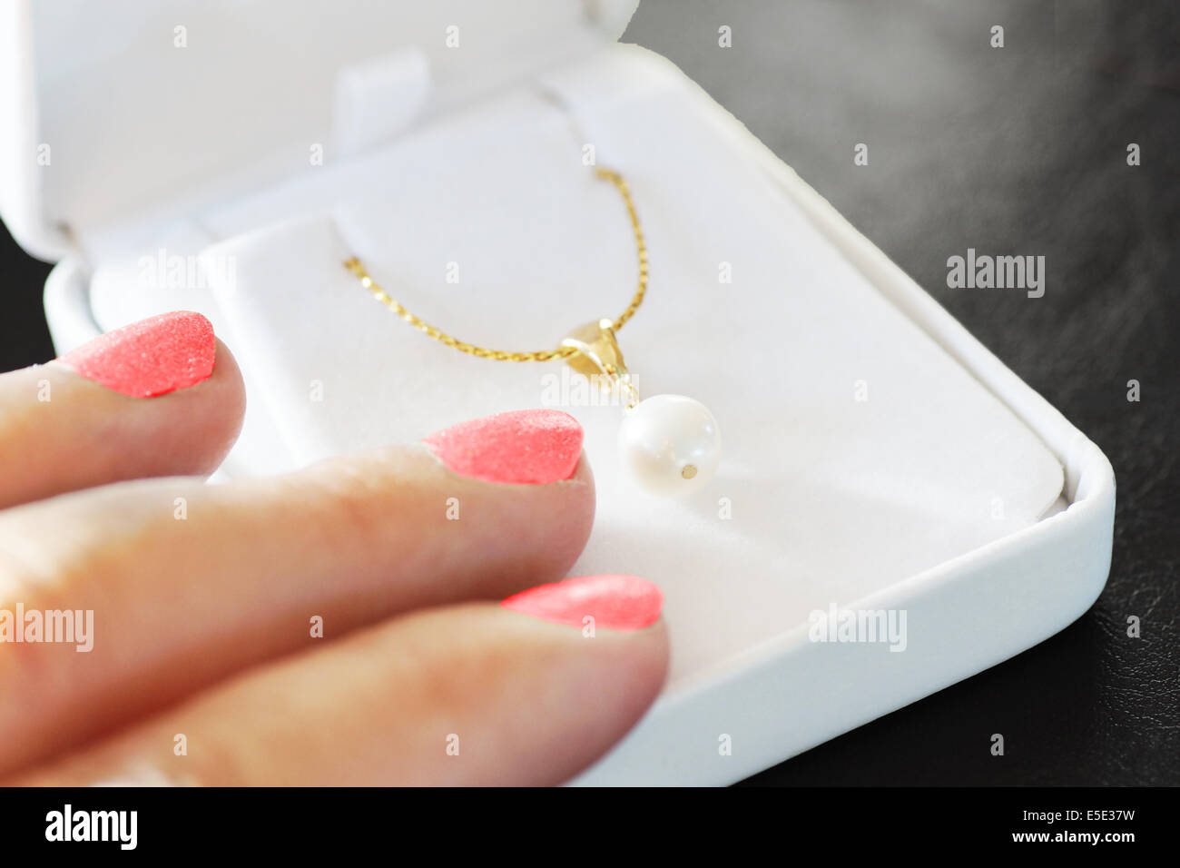 Woman fingers with pink nail polish on jewelry box with gold necklace with white pearl, gift and love concept Stock Photo
