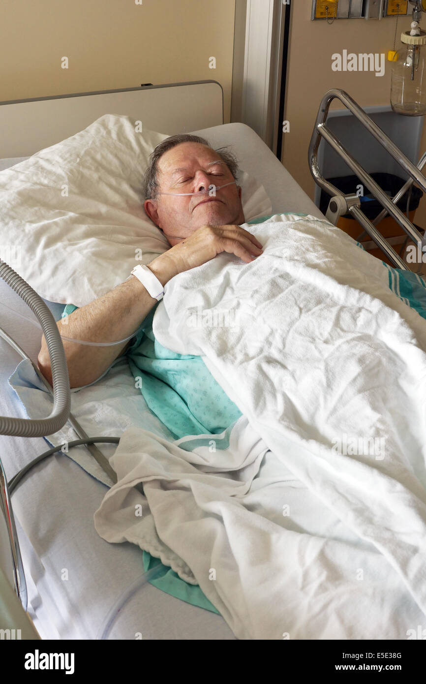 Senior man lying in hospital bed getting oxygen in intensive care unit, vertical Stock Photo