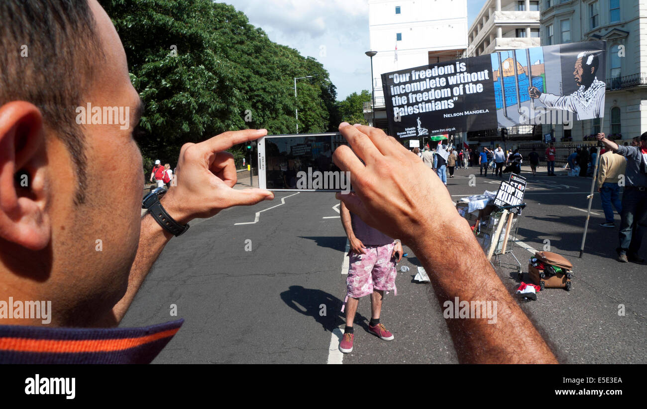 Man photographing a banner on the street at protest of bombing Gaza Palestinians by Israelis London UK  19.7.2014  KATHY DEWITT Stock Photo