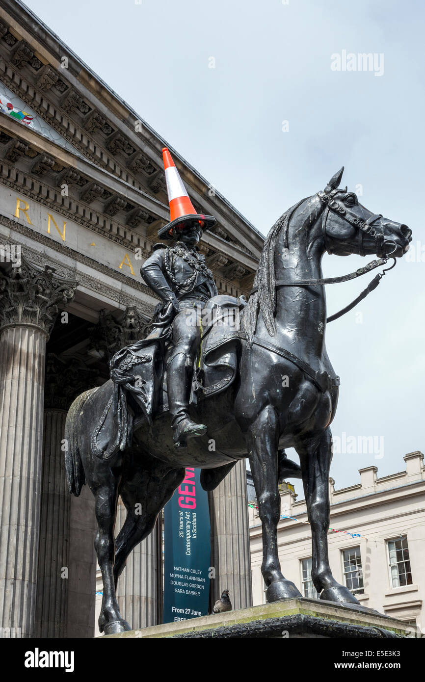 Glasgow, Scotland, UK. 29th July, 2014. Kevin Powell, a street and mime artist from Cheshire, England shows some entrepreneurship by mimicking Glasgow's iconic statue of the Duke of Wellington with a parking cone on its head by sitting on a small wooden horse in Buchanan Street pedestrian precinct. The Duke of Wellington statue is a recognisable icon of Glasgow humour and Kevin Powell's mocking created a tremendous amount of interest and laughter. A full sized replica of the statue was used during the opening ceremony of the Commonwealth Games. Credit:  Findlay/Alamy Live News Stock Photo