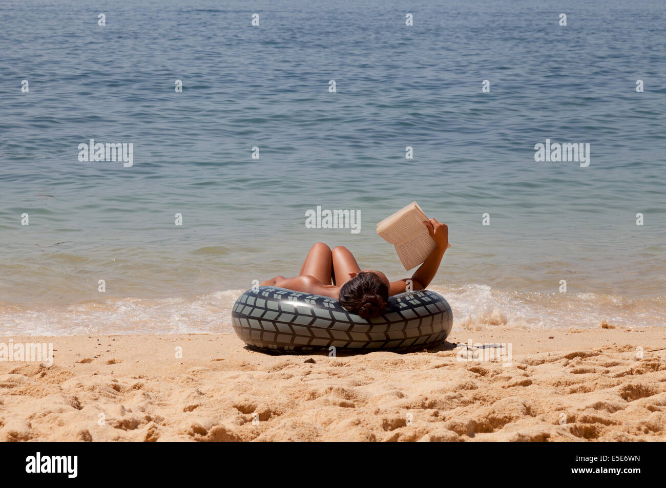 A woman relaxing and reading a book on the beach on summer holiday, Algarve, Portugal Europe Stock Photo