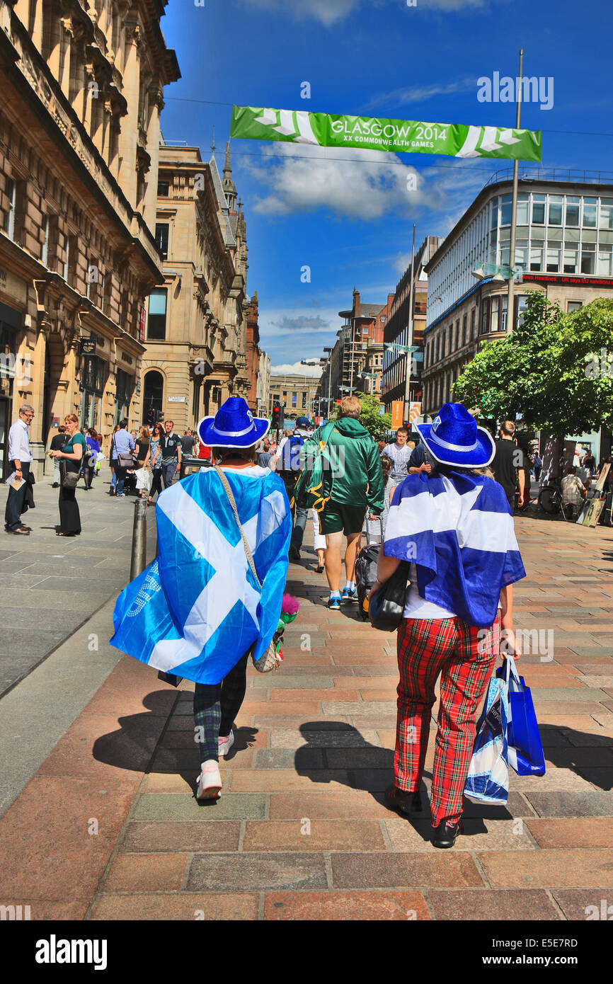 Glasgow, Scotland, UK. 28th July, 2014. Commonwealth Games supporters draped with the Scottish Flag (Saltire) and wearing tartan trousers walking through a bustling Buchanan Street in Glasgow on a scorching afternoon as games fever engulfs the city. Credit:  PictureScotland/Alamy Live News Stock Photo