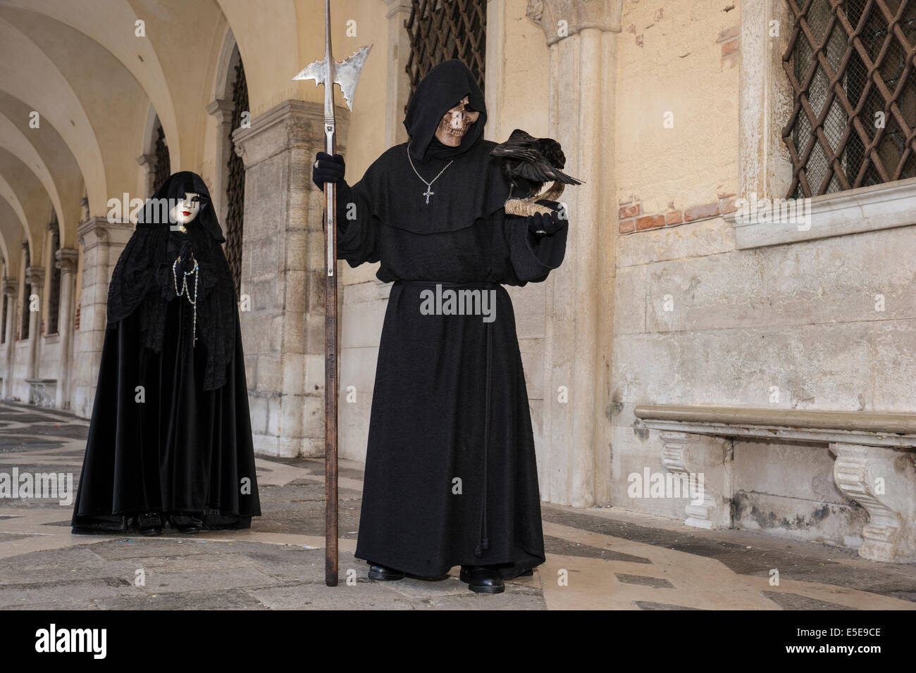 Death and his female attendant walk the colonnade of the Doge's Palace in St. Mark's Square during Carnival in Venice. Stock Photo