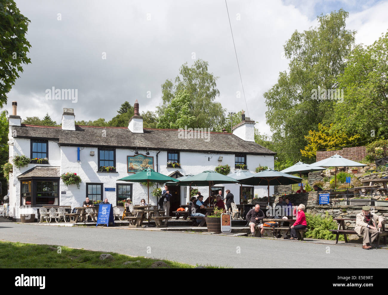 The Britannia Inn, a whitewashed free house country pub in the village of Elterwater, Lake District, Cumbria with umbrellas for outside dining Stock Photo