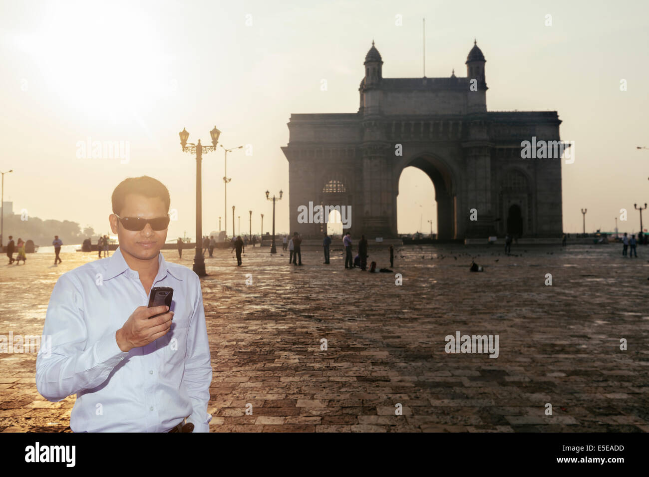 A young India man reading texts on his mobile phone with the Gateway of India behind him, Mumbai Stock Photo