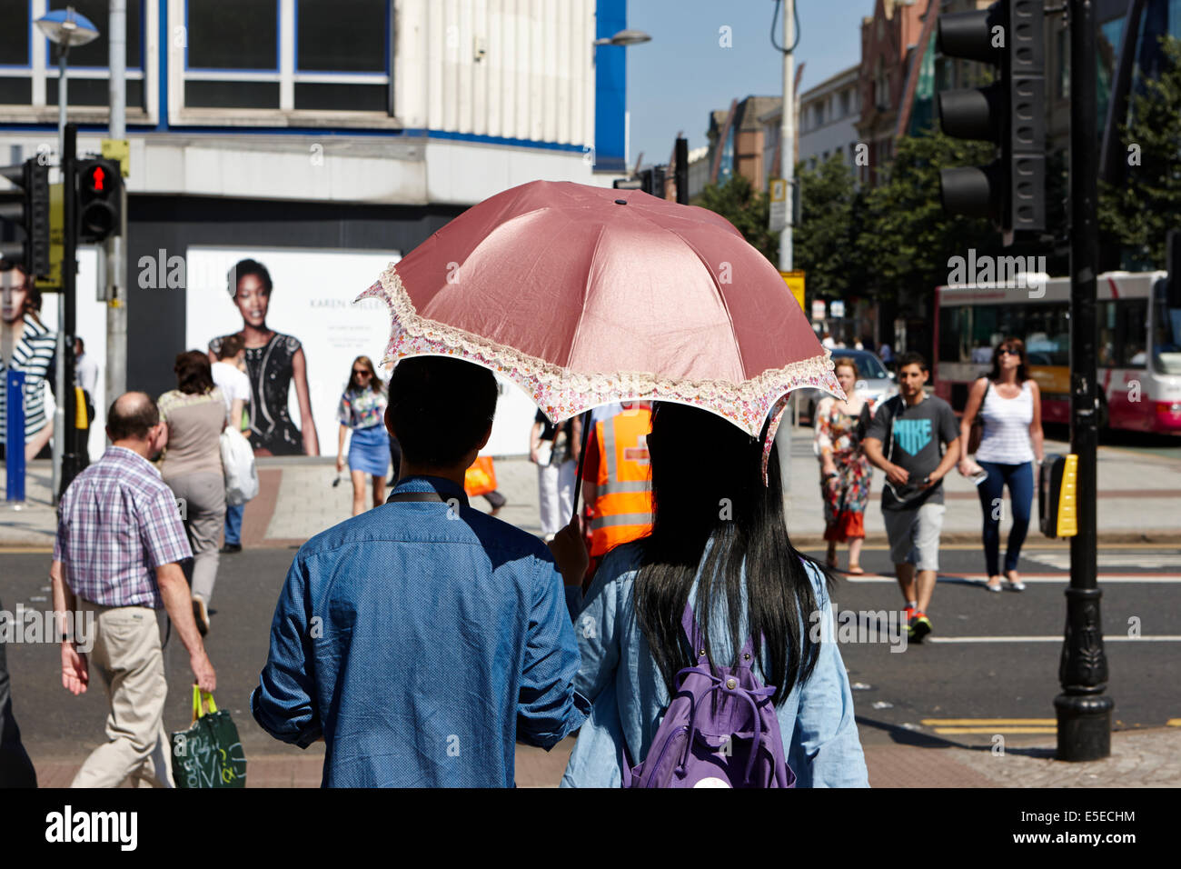 male and female asian tourist couple using a parasol on a hot sunny summers day in Belfast city centre Stock Photo