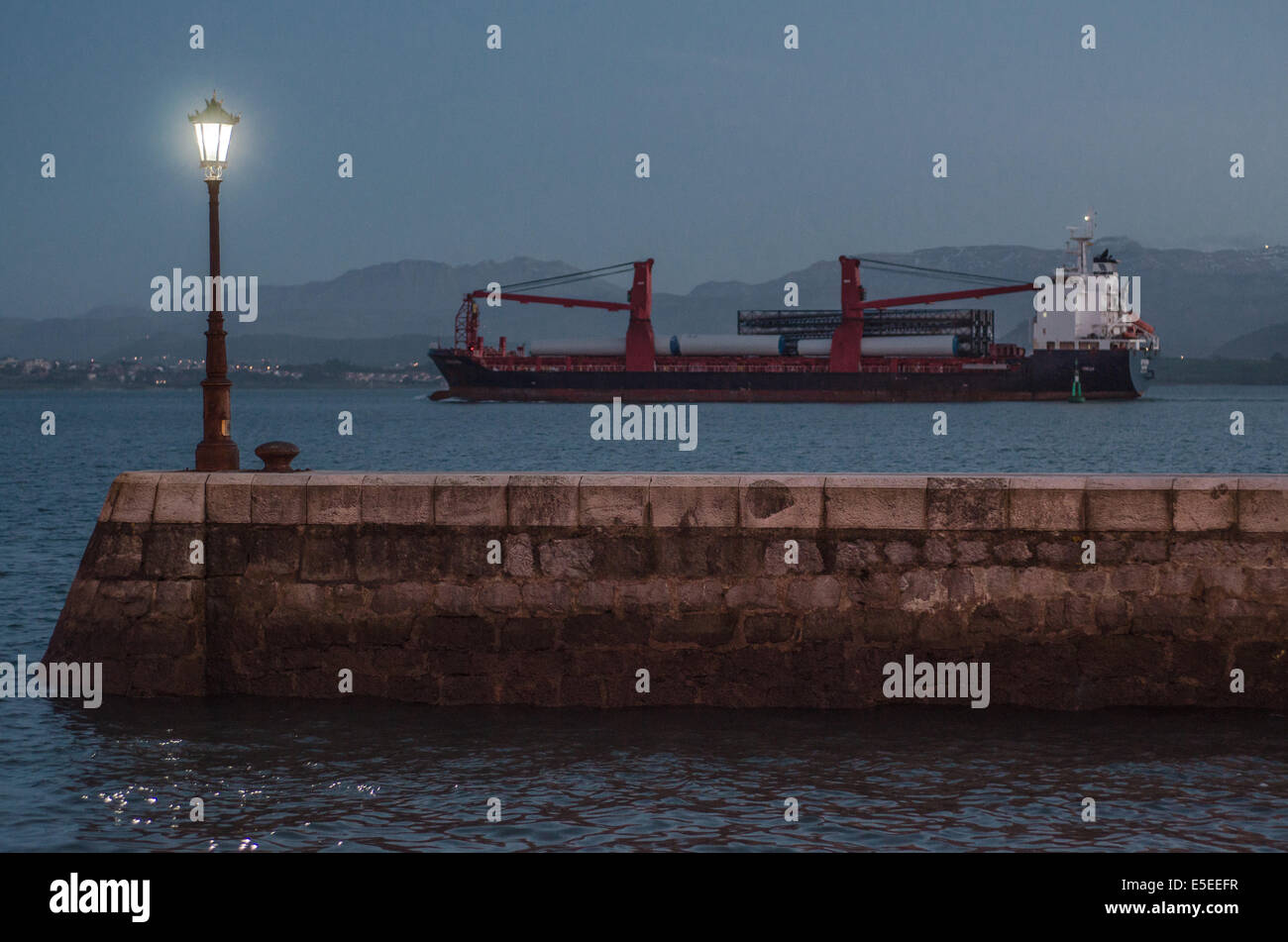 A cargo ship leaves Santander harbour in the evening. It will sail a short distance across Santander bay before reaching the ope Stock Photo