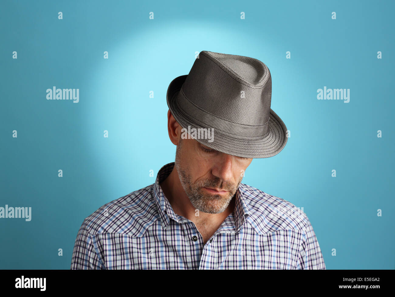 A portrait of a 40-something male wearing a fedora gazing down in thought. Stock Photo