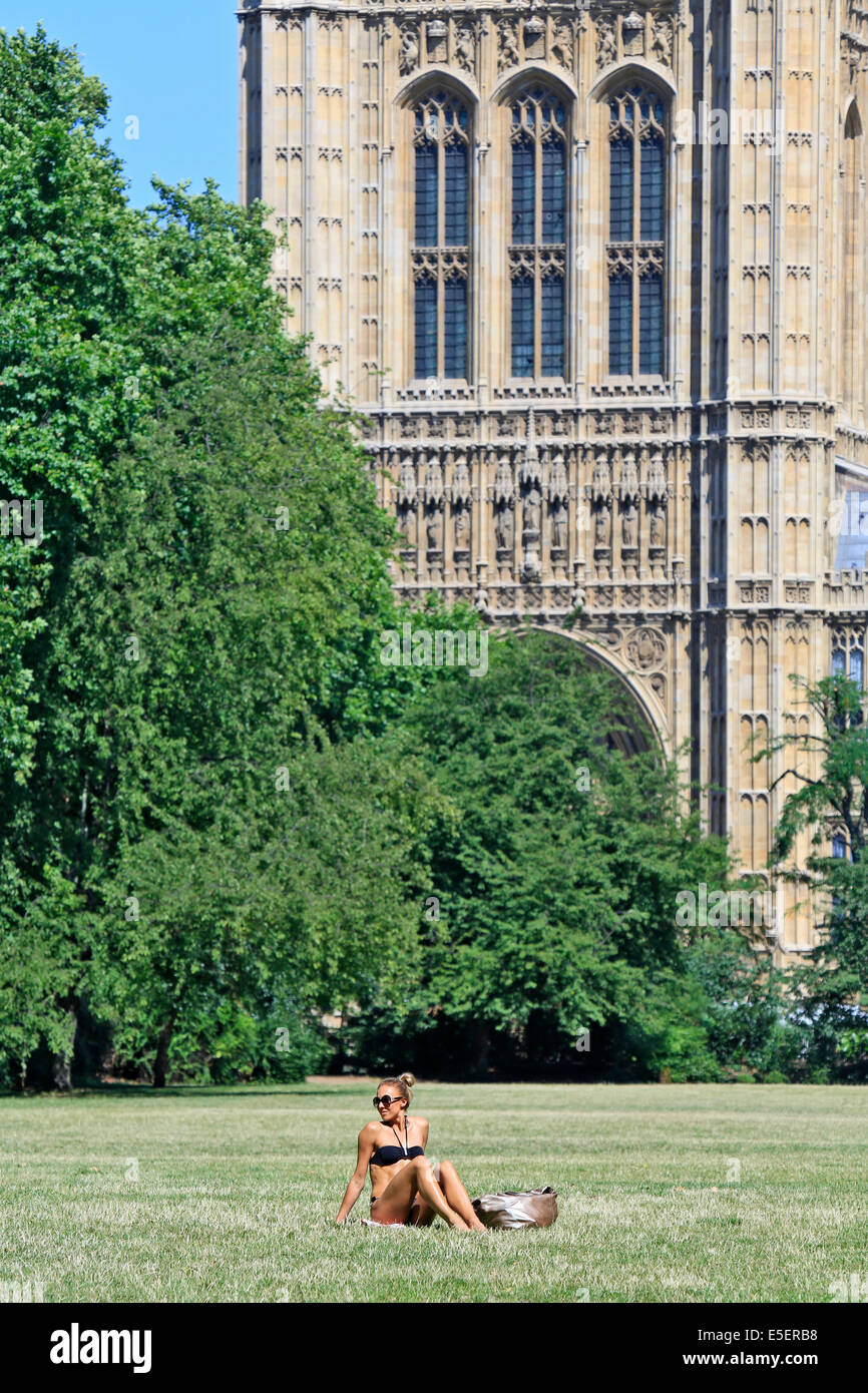 A beautiful young woman sunbathing next to the Houses of Parliament, in Victoria Tower Gardens, Westminster, London, UK Stock Photo