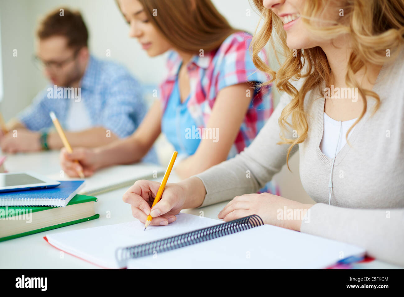 Smiling girl and her groupmates on background carrying out written task at lesson Stock Photo