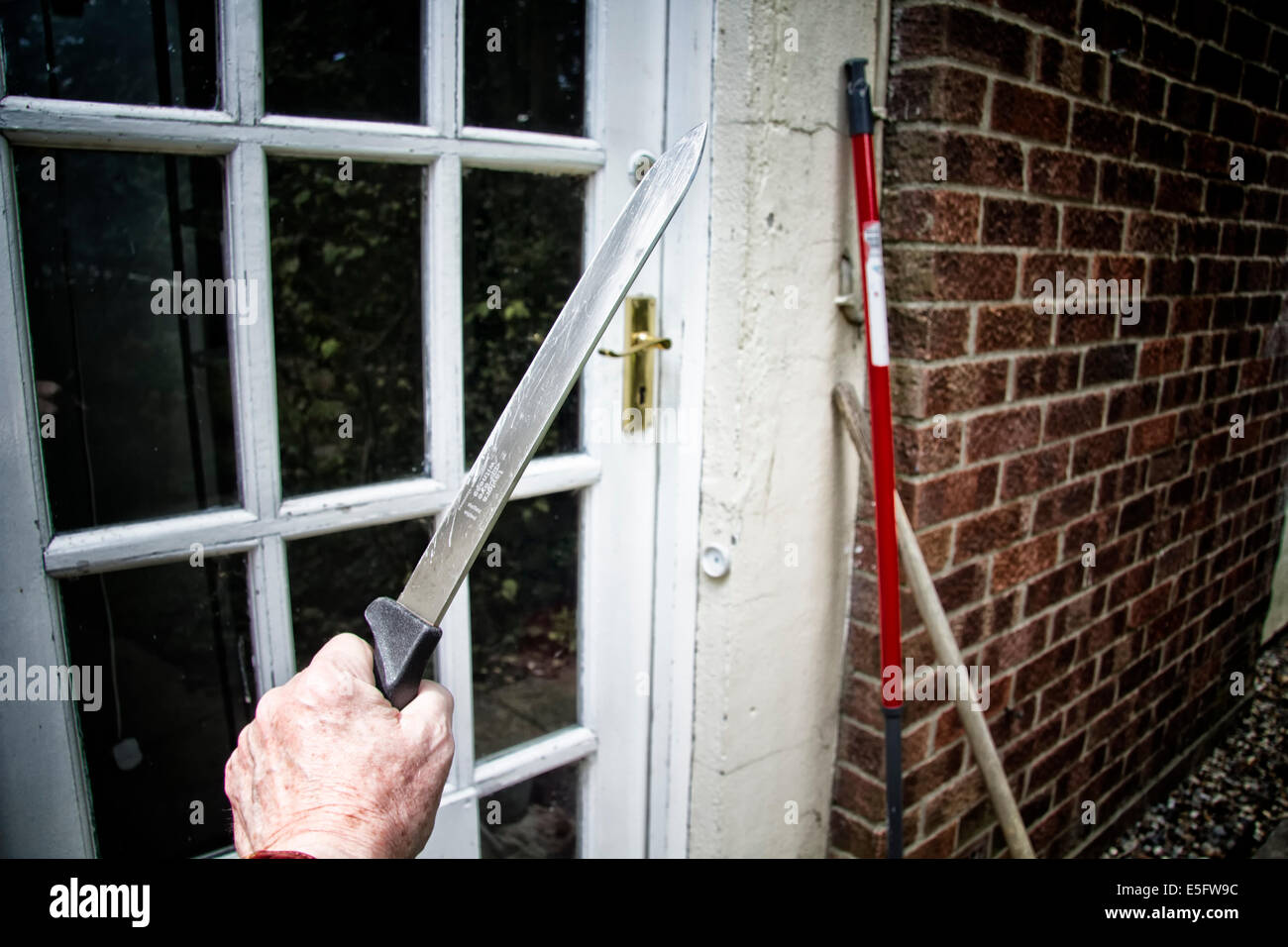 Male hand holding a large kitchen knife approaching the door to a house Stock Photo