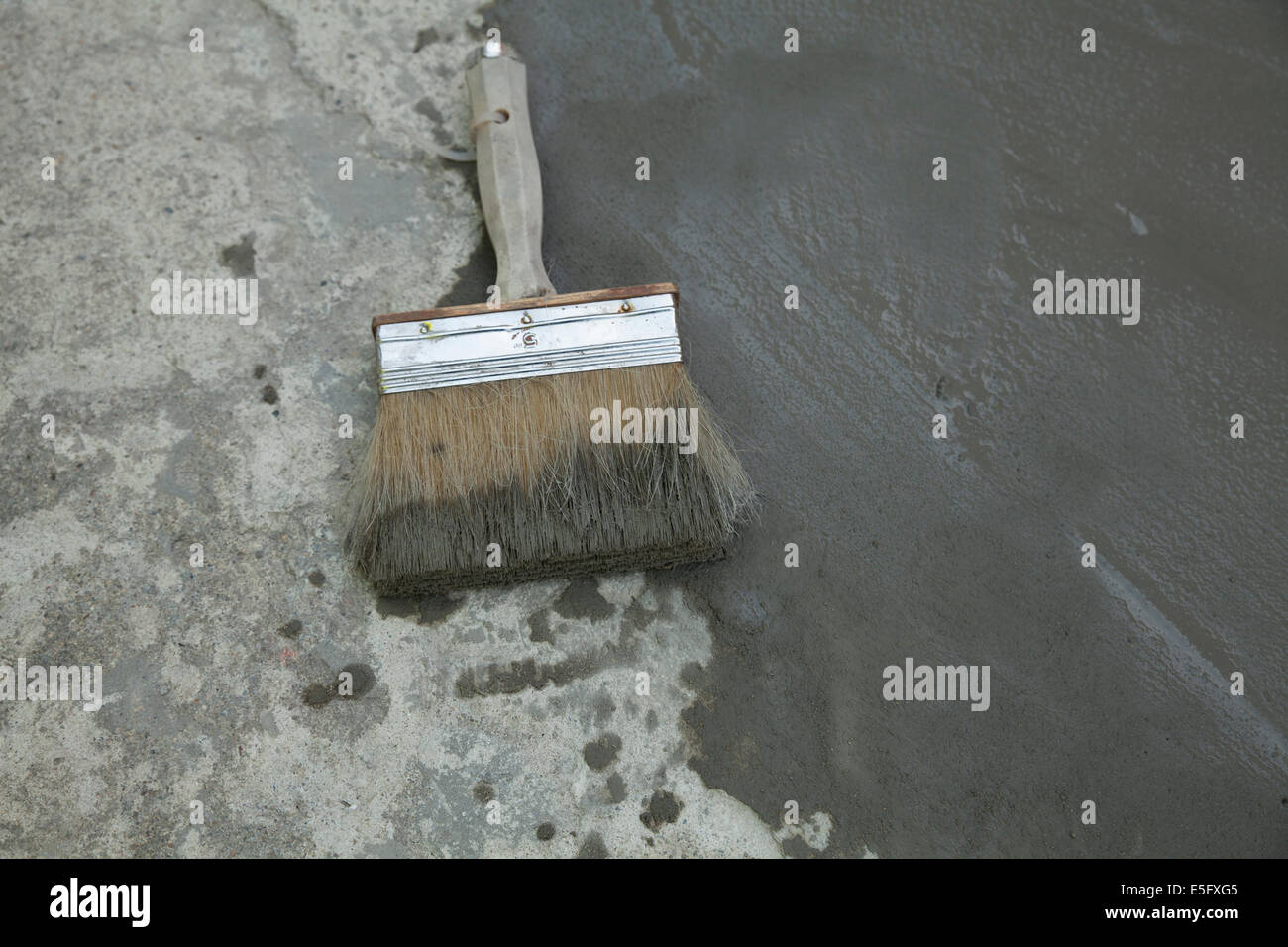 A large, coarse brush is used to smooth out a skim coat of cement to smooth an old and uneven surface. Stock Photo