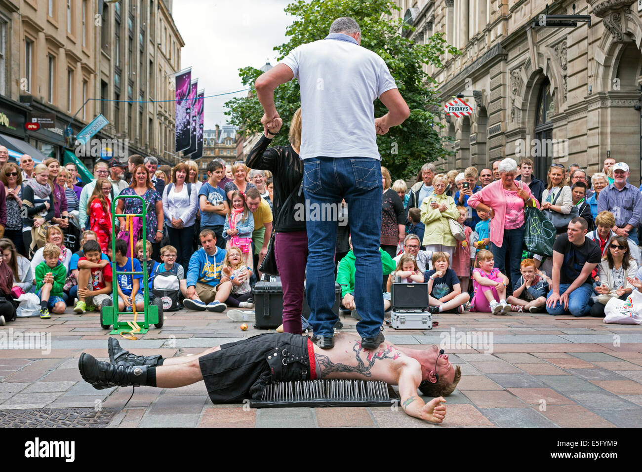 Street entertainer in Buchanan Street, Glasgow lying on a bed of nails with a member of the