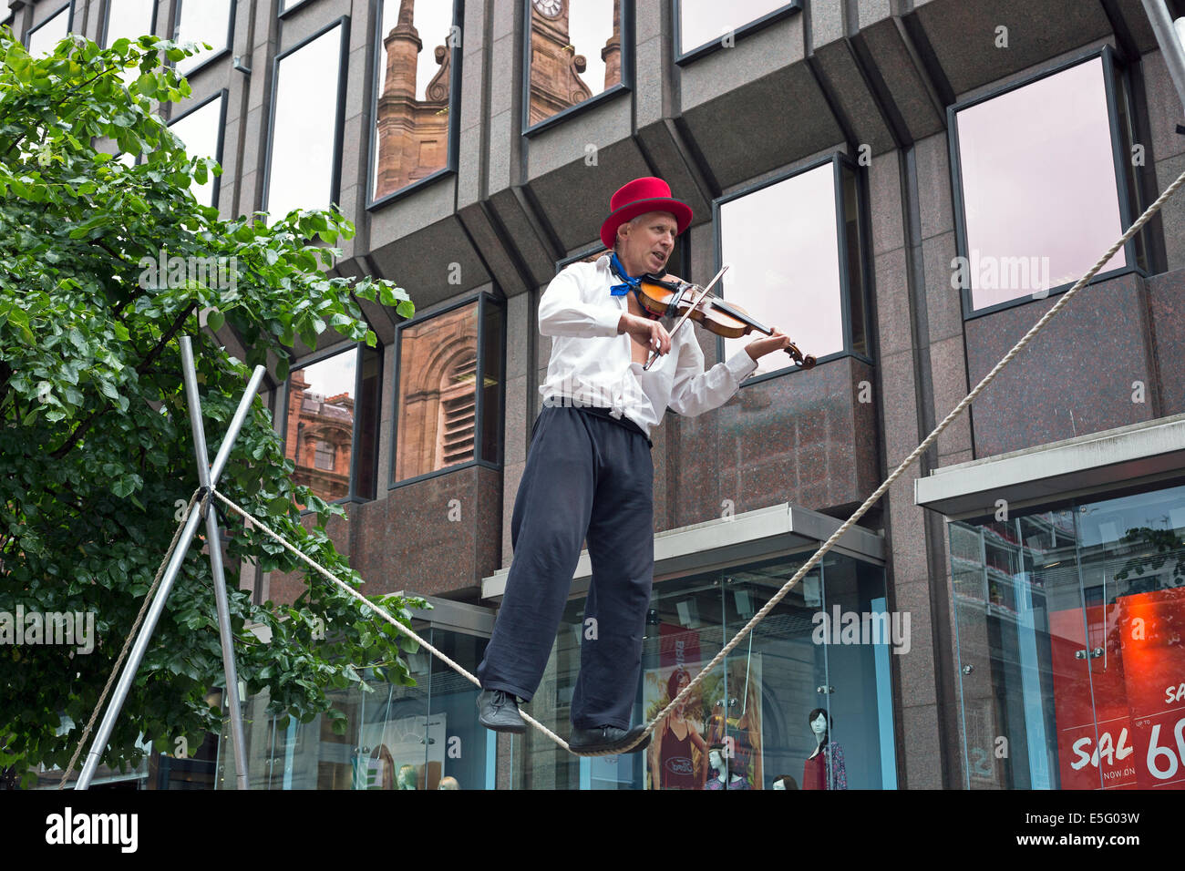 Street busker playing a violin while performing on a trapeze, Buchanan Street, Glasgow, UK Stock Photo