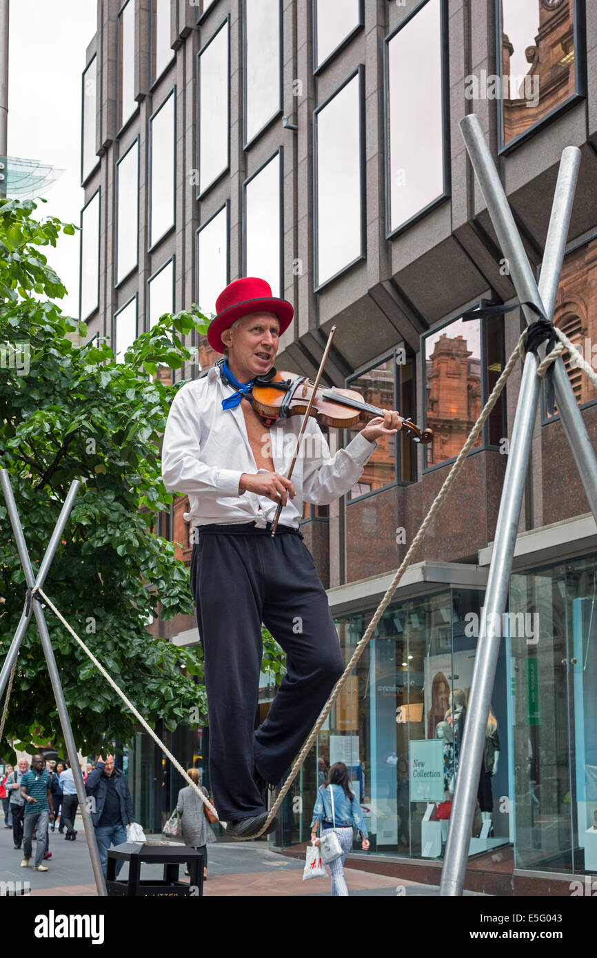 Street busker playing a violin while performing on a trapeze, Buchanan Street, Glasgow, UK Stock Photo