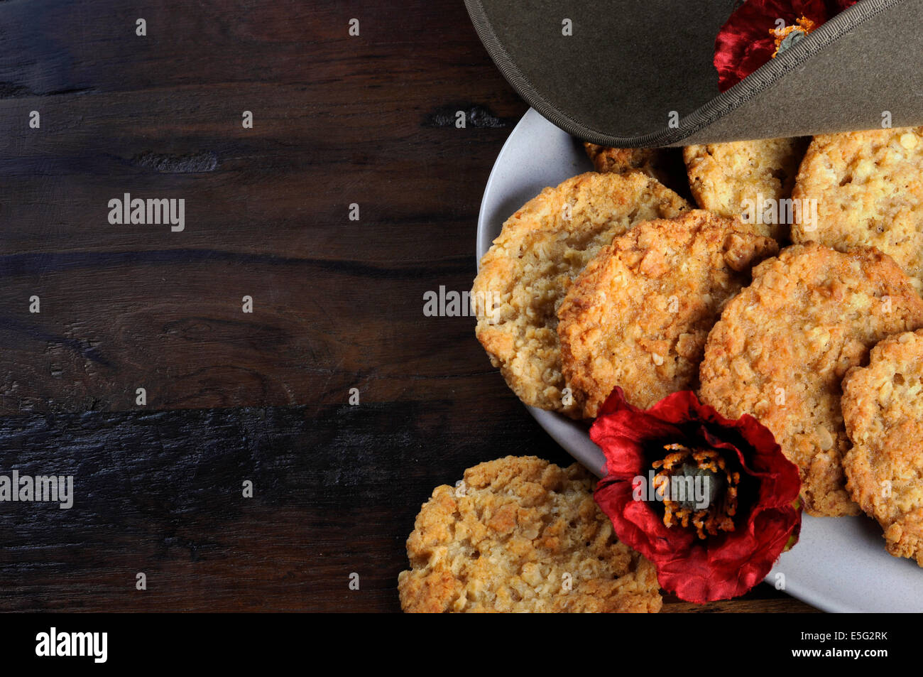 Australian army slouch hat and traditional Anzac biscuits on dark recycled wood with remembrance red poppy. Stock Photo