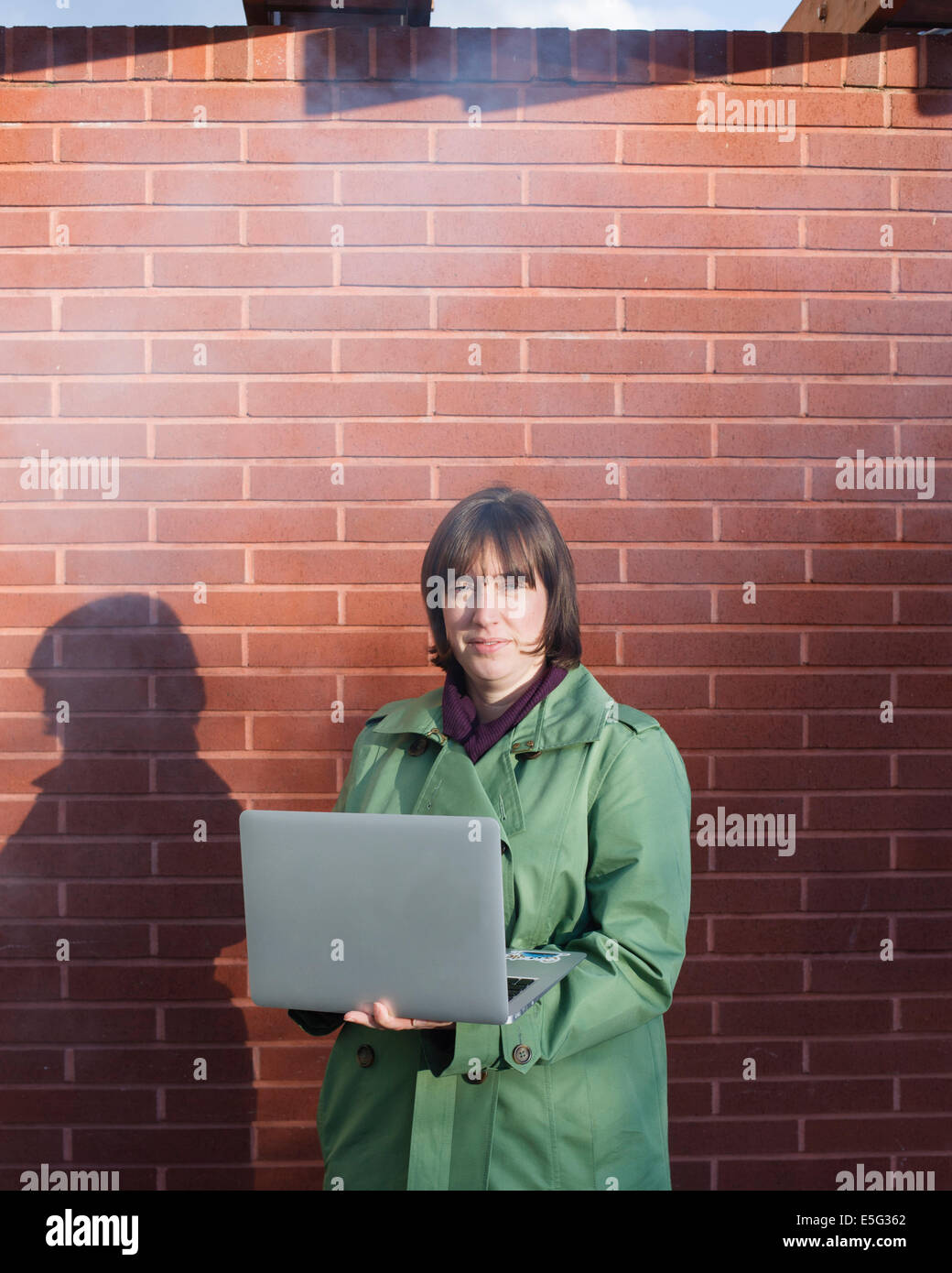 Woman with laptop standing by brick wall Stock Photo