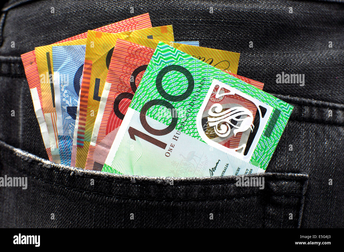 Australian money including 100, 50, 5, 10 and 20 dollar notes, in back pocket of a man's black charcoal jeans pocket. Stock Photo