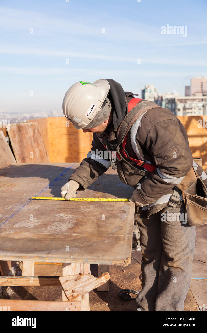 A worker measuring a piece of plywood on a rooftop construction site in Toronto, Ontario, Canada. Stock Photo