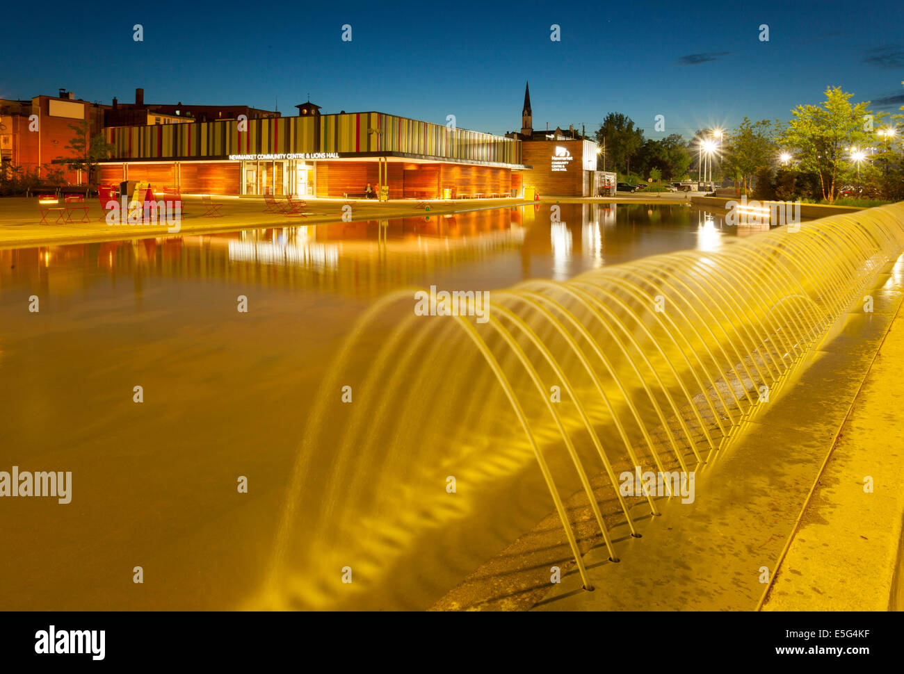 The Newmarket Community Centre with the water feature in the foreground bathed in yellow light at dusk in downtown Newmarket, On Stock Photo