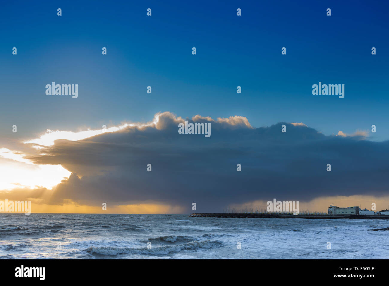 Brighton marina under a dark storm cloud and set in a rough sea with a rain squall in the distance, England, UK Stock Photo
