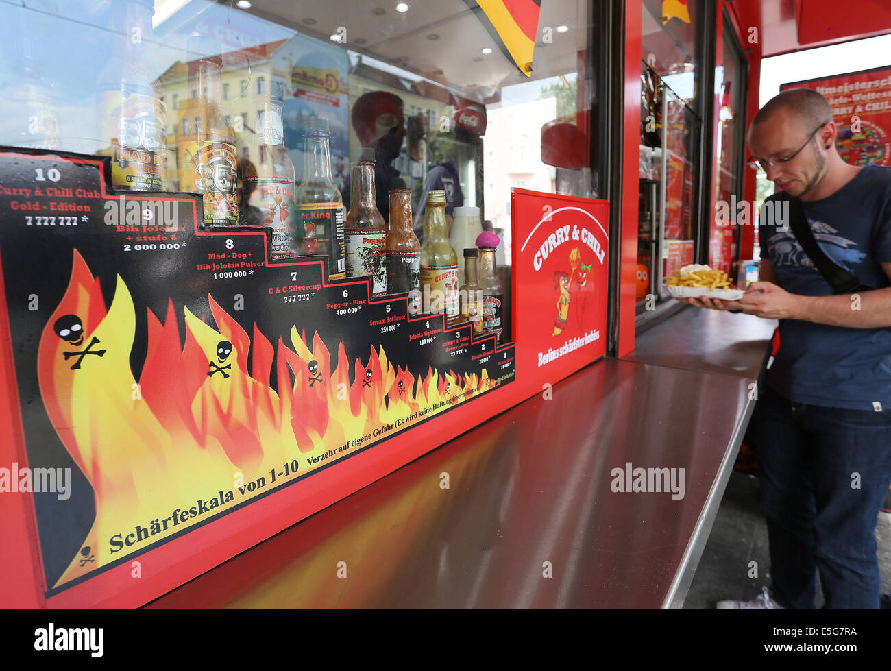 Berlin, Germany. 07th July, 2014. A young man orders a currywurst at the diner 'Curry & Chily' in Wedding in Berlin, Germany, 07 July 2014. The diner offers curry sausages in varying degrees of spiciness. Customers who eat a meal with the spiciness degree ten can become a member in the curry club and have their portrait shown at the diner. Photo: Stephanie Pilick/dpa/Alamy Live News Stock Photo