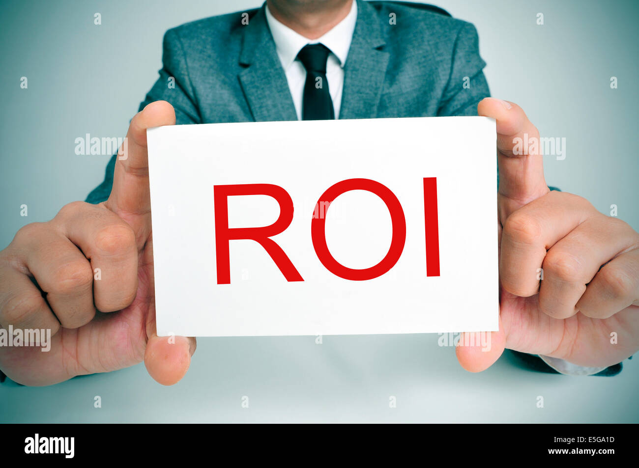 businessman sitting in a desk showing a signboard with the text ROI, ROI, acronym for Rate of Interest or Return on Investment, Stock Photo