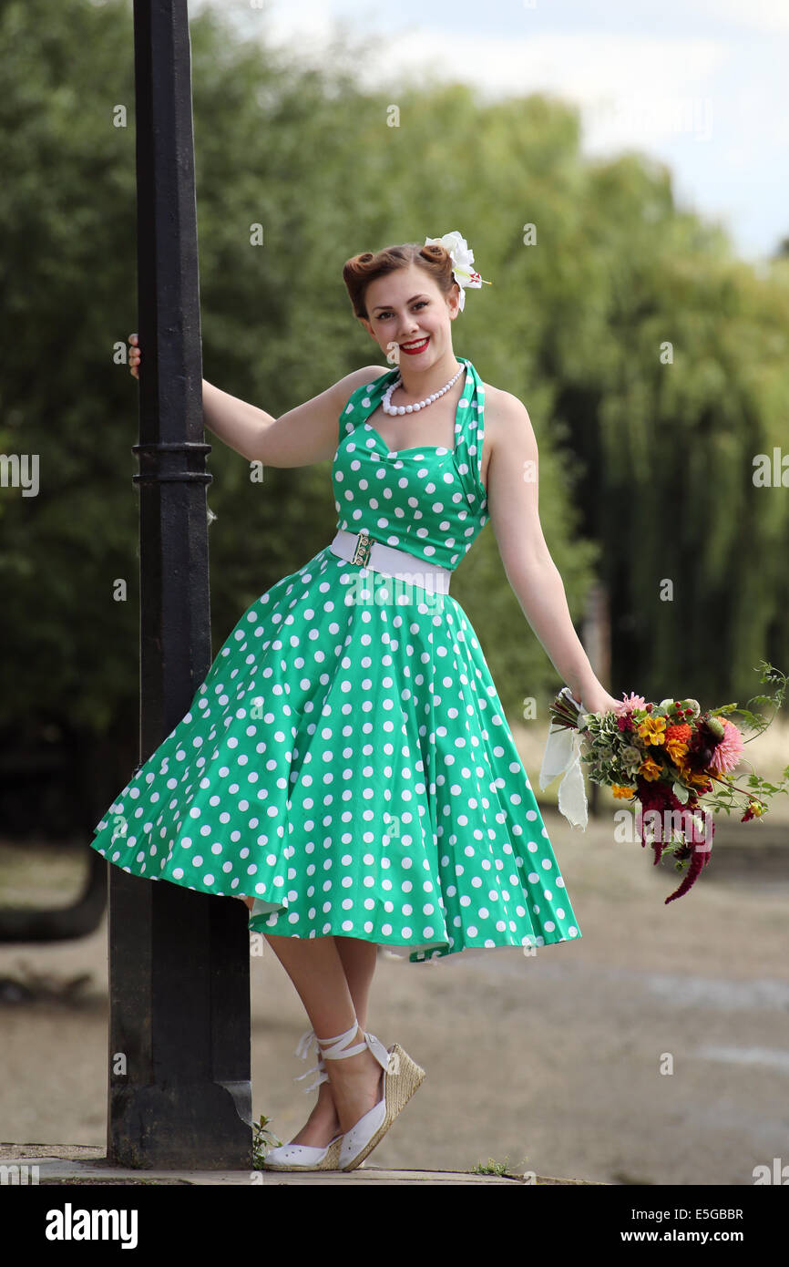 Woman in vintage polka dot dress leaning from a lamp post holding a bunch  of flowers Stock Photo - Alamy