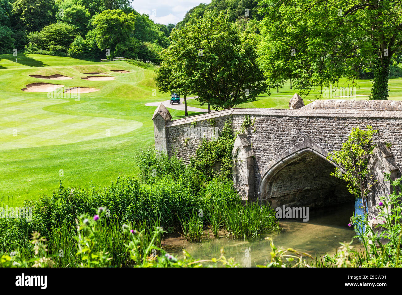 Stone footbridge over a stream through a golf course with bunkers beyond. Stock Photo